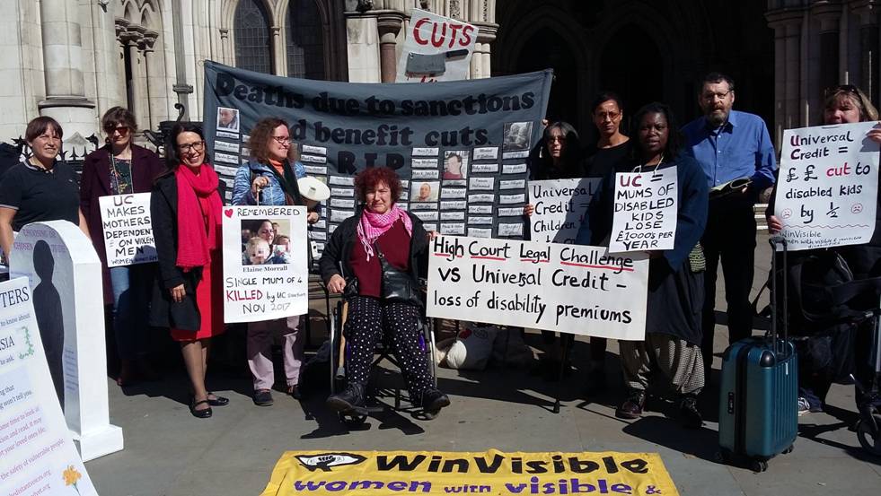 A multiracial crowd of supporters outside the High Court holding placards and a grey banner headed Deaths due to sanctions and benefit cuts -- with a list of names.