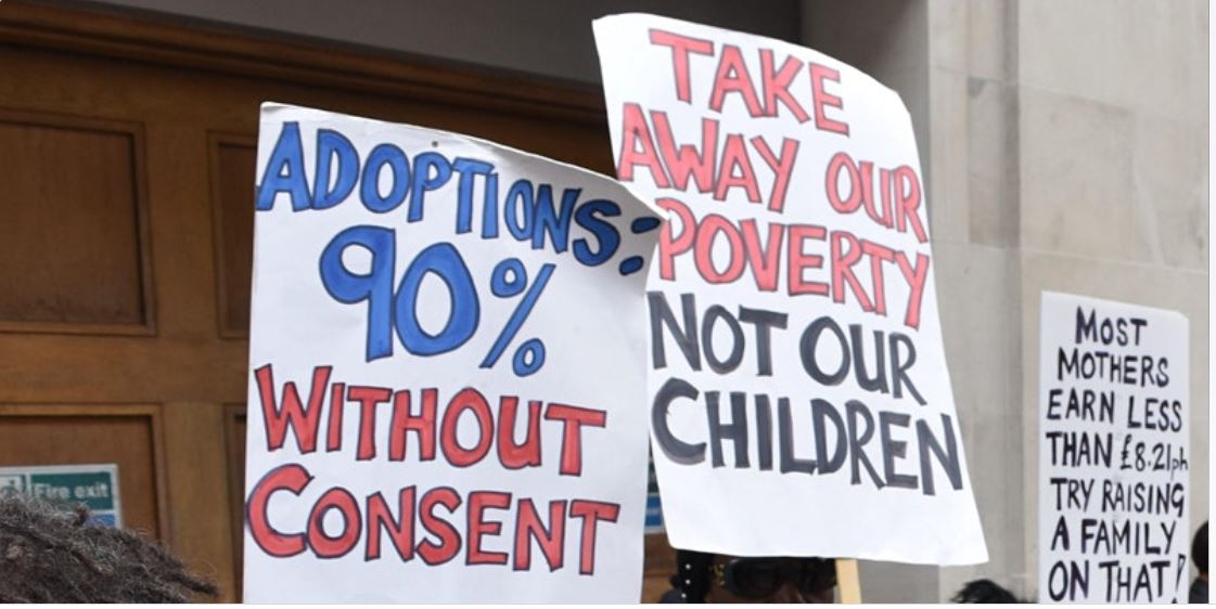 Photo from Support Not Separation's picket of the family court in Holborn, London.  Placards say: Adoptions: 90% without consent.  Take away our poverty, not our children.  Most mothers earn less than £8.21 per hour -- try raising a family on that!