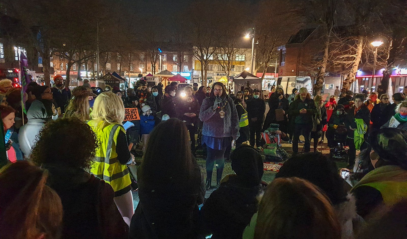 A woman on the microphone in Walthamstow Town Square, with a crowd gathered around in a circle.
