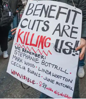 A woman holds a placard in black and red marker pen: Benefit cuts are KILLING us!!  We remember: Stephanie Bottrill.  Mark Wood.  Linda Wootton.  Cecilia Burns.  June Mitchell.  by WinVisible -- women's symbols with disabilities.