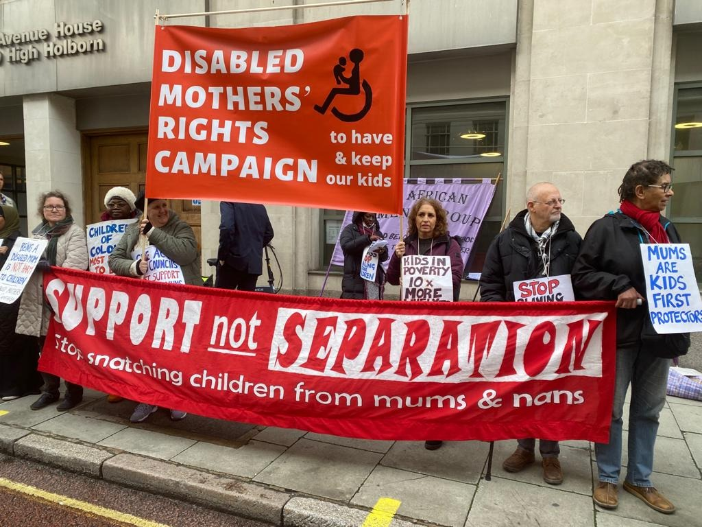People in front of the family court building hold a red banner with Support not Separation stop snatching children from mums and nans.  An orange banner reads Disabled Mothers' Rights Campaign -- to have & keep our kids.