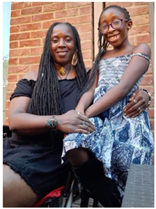 Nicole and her daughter are Afro-Caribbean.  Her daughter is perched on the arm of Nicole's wheelchair, Nicole has her arm around her, both are smiling.