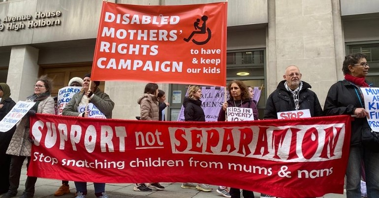 People in front of the family court building hold a red banner with Support not Separation stop snatching children from mums and nans. An orange banner reads Disabled Mothers' Rights Campaign -- to have & keep our kids.