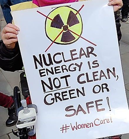 Holding a placard. A nuclear symbol is crossed out. Nuclear energy is NOT clean, green or safe! #WomenCare!