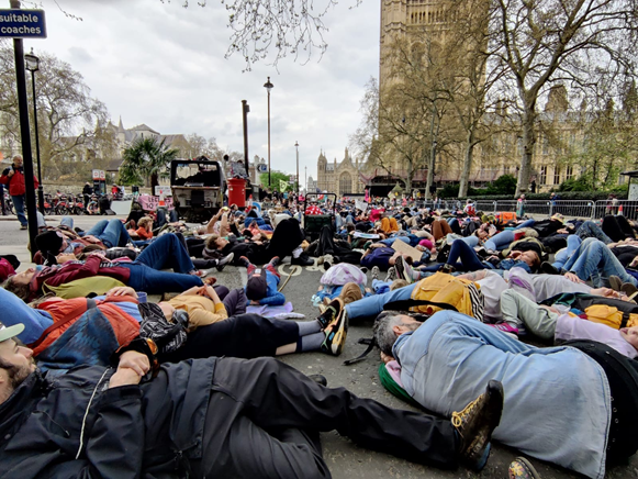 People lying in the road along Millbank. There are thousands that stretch far into the distance where buildings next to Parliament can be seen.