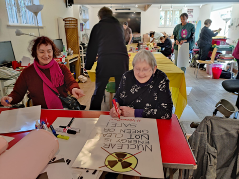 Getting ready at the Crossroads Women’s Centre.  Claire and Heulwen making placards.  Cristel and team making the Women Care yellow banner on a big table.  Behind them, Kay and team making the tabards (sleeveless tops) on sewing machines.