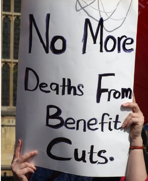 A woman holds a placard.  No more deaths from benefit cuts.