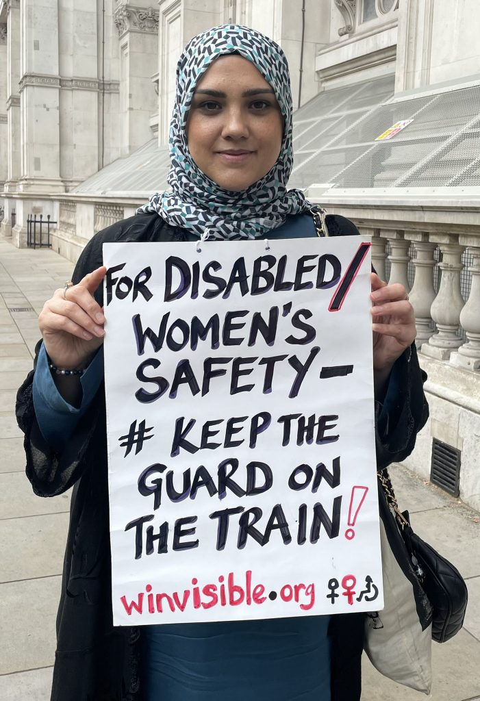 A smiling woman wearing a headscarf holds a placard, For disabled/women's safety, Keep the Guard on the Train!  winvisible.org