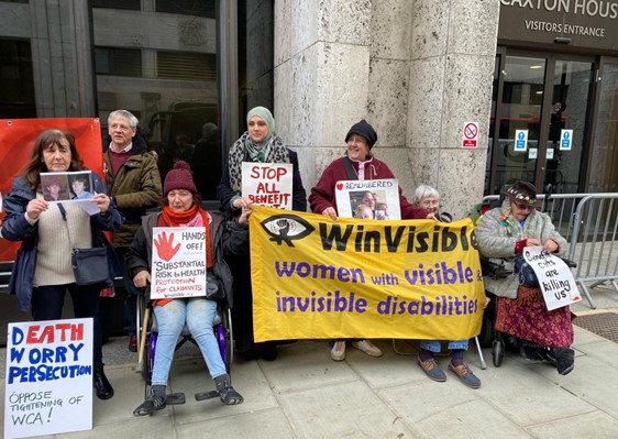 WinVisibl;e women holding the banner and placards outside the DWP building.    Tracey wears a photo of Elaine Morrall.  Other placards: Stop all benefit cuts and sanctions.  Hands off Substantial risk to health -- protection for claimants.  DWP Death Worry Persecution -- oppose tightening of WCA! Gill holds photos of her brother David Clapson.  A man holding red Unite Community banner.