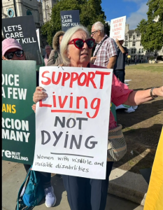 Anne Hall holds a placard, Support living not dying -- WinVisible