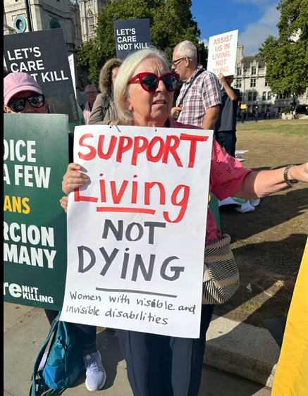 Anne Hall holds a placard, Support living not dying -- WinVisible