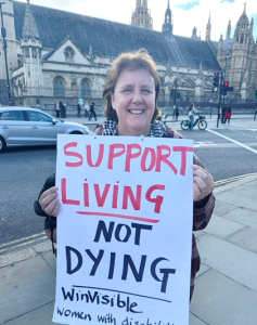 With the Houses of Parliament in the background, Tracey Norton holds a placard, Support living not dying -- WinVisible
